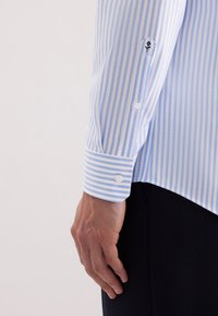  Lichtblauwe en witte gestreepte langemouwen shirt met een geknoopt manchet, met een klein geborduurd ontwerp op het manchet. Zachte stofstructuur.