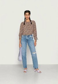 Top floral de manga longa com punhos elásticos, jeans de ganga clara com detalhes desgastados, sandálias de slide lavanda e uma bolsa lilás.