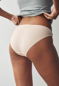Svetlo bež bombažne hlačke z gladko teksturo, ki imajo nežne valovite robove. Pogled je usmerjen od zadaj, z oblikovano zasnovo.