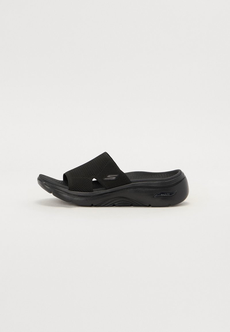 Svart glide sandal med teksturert stoffoverdel, omformet såle og polstret fotseng. Har "Arch Fit" merke på siden.