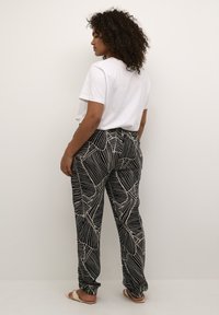 Schwarze Hose mit weißem Blattmuster, elastischem Bund, lockerer Passform, kombiniert mit einem schlichten weißen T-Shirt, von hinten betrachtet.