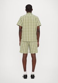 Πράσινο και λευκό καρό κοντομάνικο πουκάμισο και αντίστοιχες βερμούδες, κατασκευασμένα από ελαφρύ ύφασμα; άνετη εφαρμογή και καρό σχέδιο σε όλη την επιφάνεια.