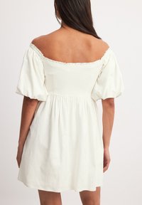 Sukienka biała, krótka, odsłaniająca ramiona, z bufiastymi rękawami, elastycznym dekoltem, marszczonym talią i rozkloszowanym dołem. Gładki bawełniany materiał.
