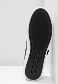 Semelle d'une sneaker noir et blanc, avec une surface texturée antidérapante, portant l'inscription "MICHAEL KORS" en relief au niveau du talon.