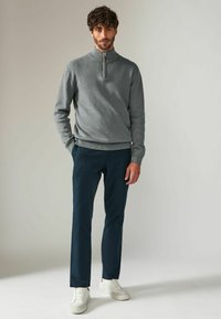 Szary rozpinany polar z miękkiego materiału, w połączeniu z granatowymi spodniami. Model stoi w białych sneakersach na jasnym tle.