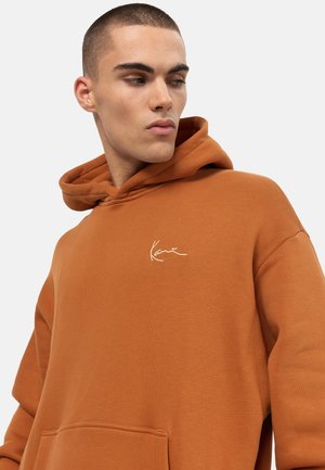 Brown hoodie made of soft fabric, featuring a kangaroo pocket and a white embroidered logo on the left chest area.