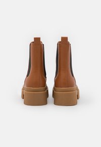 Hnědé kožené kotníkové boty s černými elastickými postranními panely a robustními béžovými platformovými podrážkami. Design obsahuje poutka na zadní straně.
