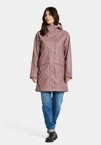 Vattentät mauve regnrock med hög krage, justerbar huva, sidofickor och rak skärning. Används över blå jeans och svarta stövlar.