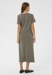 Siva, kratko rukava, dolga obleka iz mehkega blaga, s preprostim krojem in detajlom po zadnjem šivu. Oblečena s črnimi balerinkami.