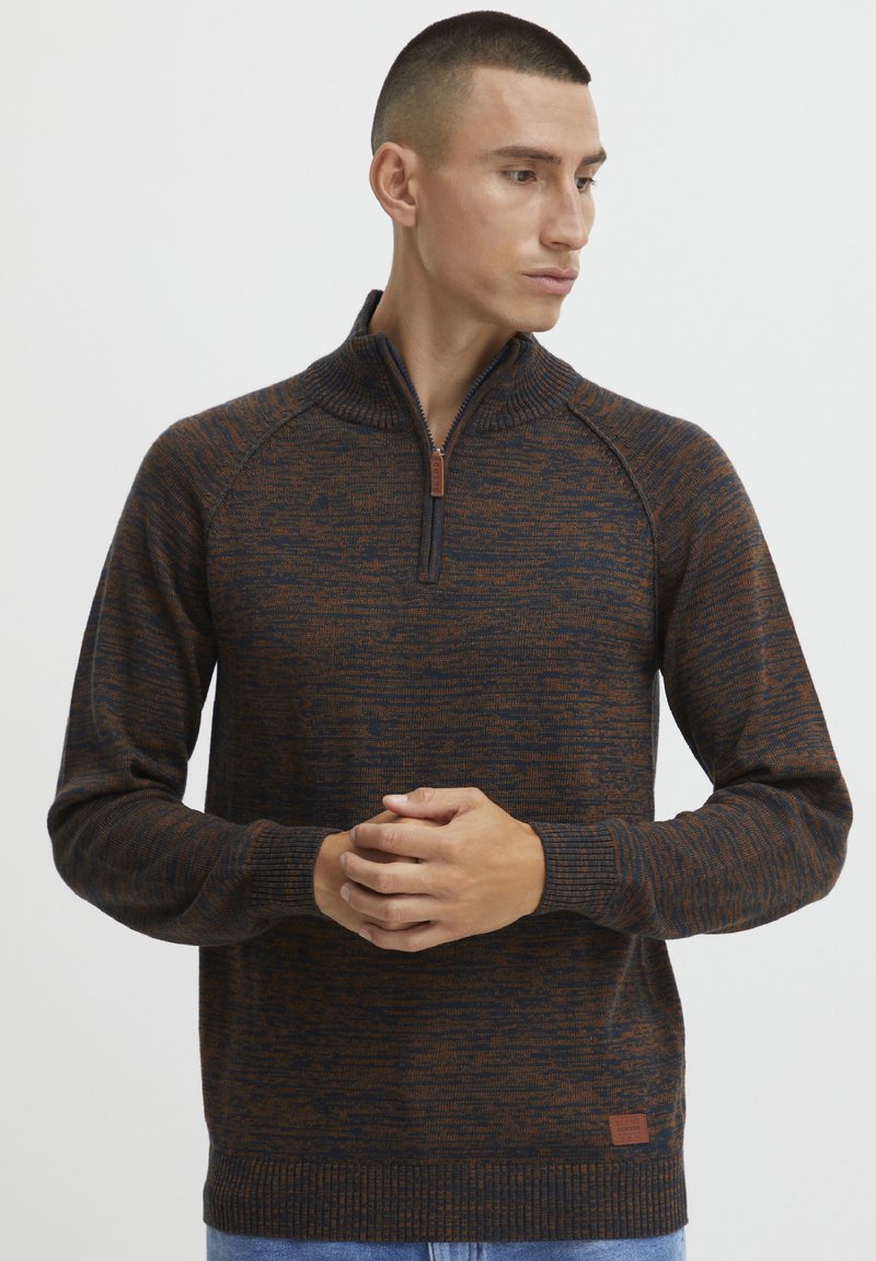 Maglione lavorato a maglia blu scuro e arancione con colletto a zip a quarto, polsini e orlo a coste; presenta una patch con logo in basso a sinistra.