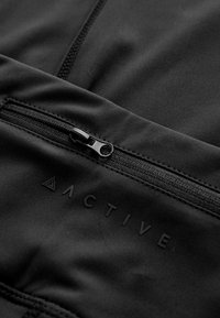 Tissu de vêtements de sport noir avec une petite poche zippée et un logo en relief. Texture lisse avec des coutures plates et un design épuré.