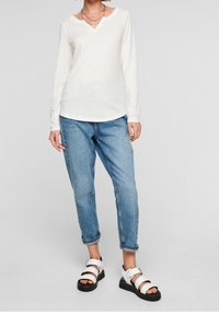 Vit långärmad t-shirt med v-ringning, avslappnad passform, matchad med ljusblå jeans och vita sandaler med svarta sulor och justerbara remmar.