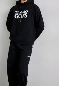 Czarna bluza z kapturem z białym napisem "TI AMO GCOS", zestawiona z czarnymi spodenkami dresowymi z małą białą naszywką z logo na udzie.