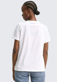 Weißes Baumwoll-T-Shirt mit kurzen Ärmeln, lockerer Passform und Rundhalsausschnitt. Flache Nähte und minimalistisches Design, kombiniert mit blauen Denim-Jeans.