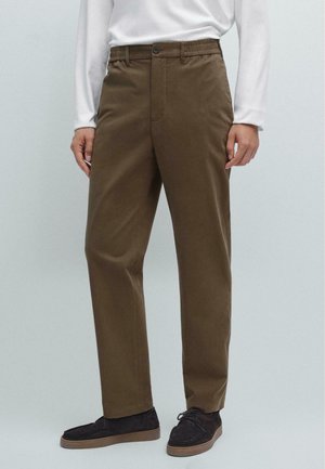 Bruine katoenen broek met eenRelaxed fit, elastische band, voorzakken en een enkele knoopsluiting, gecombineerd met donkere schoenen.