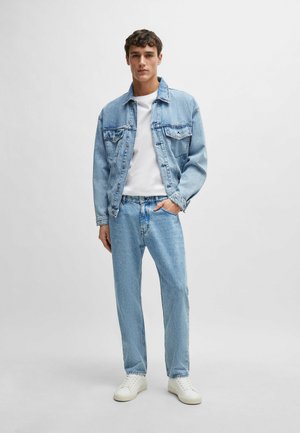 Chaqueta de mezclilla azul claro con bolsillos en el pecho, combinada con jeans azul claro a juego y zapatillas blancas. Camiseta blanca sencilla debajo.