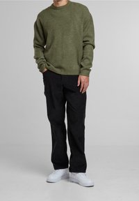 Olivově zelený pletený svetr s kulatým výstřihem, dlouhými rukávy a žebrovanými manžetami, doplněný černými manšestrovými kalhotami a bílými teniskami.