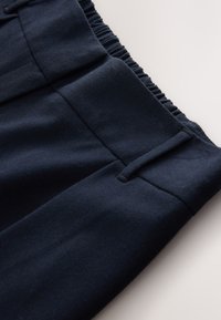 Tengerészkék nadrág sima textúrával, elasztikus derékpánttal és strukturált eleji redőkkel. Oldalzsebekkel és tiszta varratokkal rendelkező darab.