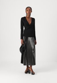 Top lungo a maniche nere avvolgente abbinato a una gonna maxi plissettata metallica. Sandali platform neri e una piccola borsa nera completano l'outfit.