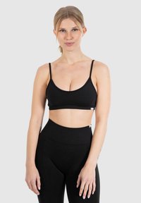 Sort bralette lavet af blødt stof med tynde justerbare stropper og et enkelt design. Har et logo-tag nederst til venstre.