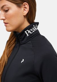 Giacca nera zip-up realizzata in tessuto liscio, con colletto alto e logo "Peak" in bianco, e un piccolo logo argentato sul lato sinistro.