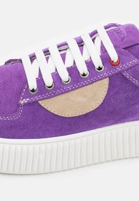 Baskets en daim violet avec une accent en daim beige, dotées de lacets blancs, d'œillets en métal et d'une semelle en caoutchouc blanc texturé.