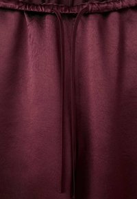 Gros plan sur une ceinture élastique bordeaux avec un cordon assorti sur un pantalon ou un short en tissu doux.