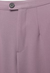 Ceinture boutonnée et braguette d'un pantalon mauve avec des coutures apparentes et un détail de poche sur le côté droit.