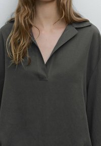 Chemise gris foncé à col avec un col en V, coupe ample et texture douce ; présente des épaules tombantes et un design minimaliste.