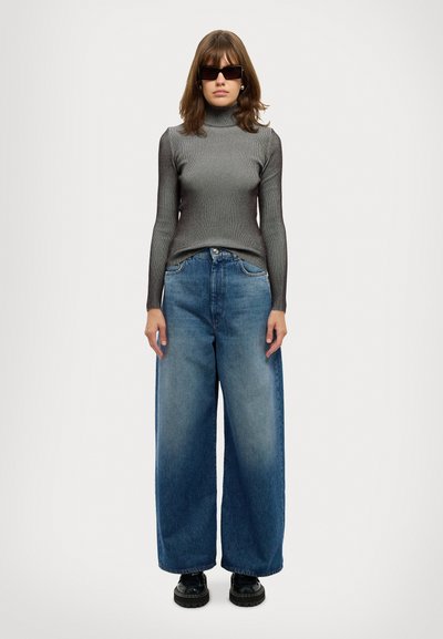 Haut à col roulé gris à côtes, jean en denim bleu clair à jambes larges et chaussures noires. La tenue se compose d'un haut ajusté et d'un pantalon volumineux.