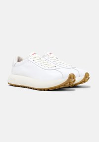 White leather sneakers with round toe, contrasting light rubber sole, and subtle logo detail in red on the tongue. Textured tread pattern.
