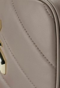 Sezione di una borsa in pelle beige con cuciture diagonali, caratterizzata da un accento metallico. Texture liscia, bordi arrotondati e linee pulite.