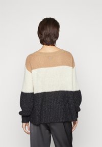 Pull en tricot épais avec des rayures horizontales beige, crème et marine foncé. Coupe surdimensionnée avec des manches amples et des poignets côtelés.