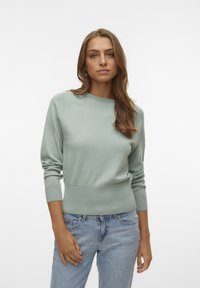 Un pull vert clair avec un col rond, des poignets côtelés et un ourlet côtelé. Fabriqué en tissu doux, il présente une coupe décontractée. Associé à un jean bleu clair.