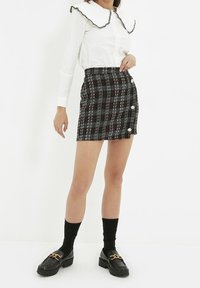 Svart och röd rutiga mini kjol med sidoknappar, kombinerad med en vit blus med en rullkrage. Bärs med svarta strumpor och loafers.