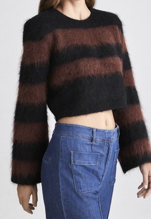 Krótki, puszysty sweter z szerokimi, poziomymi czarnymi i brązowymi paskami, zestawiony z wysokim stanem niebieskich dżinsów z dużymi przednimi kieszeniami.