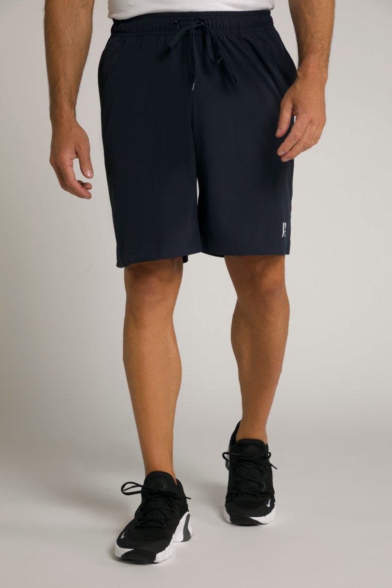 Mann trägt schwarze Sportshorts und schwarze Laufschuhe, steht vor einem neutralen Hintergrund.