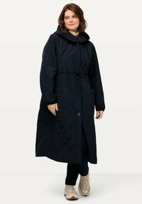 Quiltad marinblå lång kappa med huva, som har dragsko i midjan, knappstängning och sidofickor. Mjukt tyg med en släta yta.