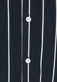 Navy button-up shirt with thin white vertical stripes, featuring a round, four-hole button and smooth fabric texture.