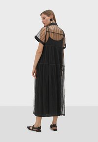 Robe noire avec une superposition transparente, au design superposé et aux manches courtes et structurées. Présente des rayures verticales et une silhouette fluide et texturée.
