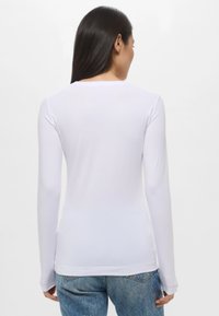 Camicia bianca a maniche lunghe realizzata in tessuto liscio con un design aderente, caratterizzata da un colletto arrotondato e orlo standard.