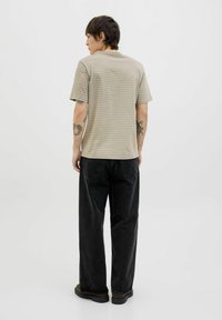 Striped, short-sleeve, beige t-shirt featuring a rounded neckline, paired with loose-fitting, dark denim jeans and black footwear.