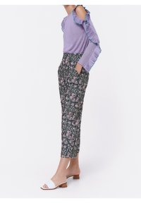 Ljuslila topp med volangdetaljer på axlarna och turkosa accenter, kombinerad med mörka blommönstrade korta byxor och vita slip-in-sandaler.