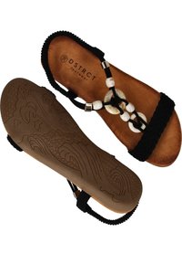 Des sandales noires tressées avec une semelle intérieure en simili cuir, présentant un motif ondulé texturé sur la semelle et des accents décoratifs en coquillage blanc.