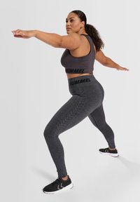 Grå sportbh och leggings med svarta detaljer och ett mönster av däckspår. Svarta träningsskor kompletterar sportklädesensemblet.