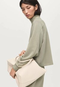 Sudadera de un suave verde oliva claro con cuello alto, corte suelto y tejido suave; bolso grande color crema con textura lisa y forma estructurada.