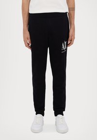 Svarta sweatpants i bomullsblandning, med slim fit, elastisk midja och kontrasterande vitt logotryck på vänster lår.