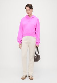Hanorac scurt roz strălucitor cu logo-ul "GAP", pantaloni bej drepți, adidași crema și o geantă mică maro. Texturi netede pe tot parcursul ținutei.