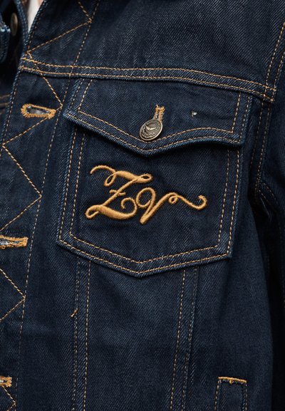 Τζιν μπουφάν με χρυστή ραφή, που διαθέτει τσέπη στο στήθος και κεντημένο λογότυπο «ZV» με καλλιγραφικά γράμματα. Μεταλλικό κουμπί στην τσέπη.