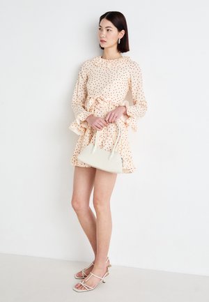 Kreemivärvi kleit punaste täppidega, volangkäised, vöödiga talje; koos väikese valge käekotiga ja palja jalanõudega.